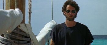 Movie still from “Jaws: The Revenge” (1987), directed by Joseph Sargent – A man in sunglasses standing on top of a sailboat; Medium shot, Low angle