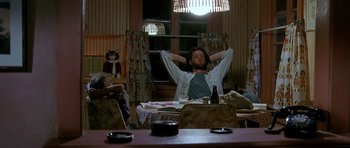 Movie still from “Jaws: The Revenge” (1987), directed by Joseph Sargent – A man sitting at a dining room table with his hands behind his head; Wide shot, Low angle