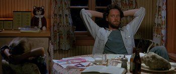 Movie still from “Jaws: The Revenge” (1987), directed by Joseph Sargent – A man sitting at a table with his hands behind his head; Medium shot, High angle