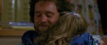 Movie still from “Jaws: The Revenge” (1987), directed by Joseph Sargent – A man with long hair and a beard is holding a dog; Close Up shot, Over the shoulder angle