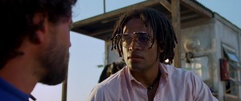 Movie still from “Jaws: The Revenge” (1987), directed by Joseph Sargent – A man with dreads wearing glasses and a pink shirt; Close Up shot, Low angle