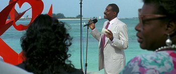 Movie still from “Jaws: The Revenge” (1987), directed by Joseph Sargent – A man in a white suit is holding a microphone; Medium shot, Over the shoulder angle