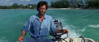 Movie still from “Jaws: The Revenge” (1987), directed by Joseph Sargent – A man sitting on the back of a boat in the water; Medium shot, Low angle
