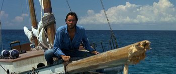 Movie still from “Jaws: The Revenge” (1987), directed by Joseph Sargent – A man sitting on the deck of a sailboat in the ocean; Medium shot, Low angle