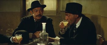 Movie still from “Jean de Florette” (1986), directed by Claude Berri – Two men are sitting at a table with a drink; Medium shot, Low angle
