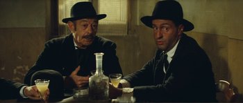 Movie still from “Jean de Florette” (1986), directed by Claude Berri – A couple of men sitting at a table with a drink; Medium shot, Low angle