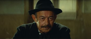 Movie still from “Jean de Florette” (1986), directed by Claude Berri – An older man wearing a black hat and a black tie; Close Up shot, Low angle