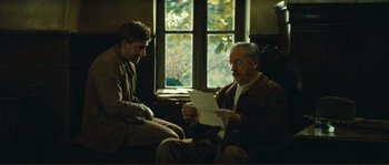 Movie still from “Jean de Florette” (1986), directed by Claude Berri – Two men sitting in front of a window looking at a piece of paper; Medium shot, Over the shoulder angle