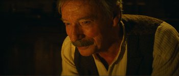 Movie still from “Jean de Florette” (1986), directed by Claude Berri – An older man with a mustache is sitting in a dark room; Close Up shot, Over the shoulder angle