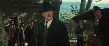 Movie still from “Jean de Florette” (1986), directed by Claude Berri – An older man in a black hat and a black coat; Medium shot, Low angle