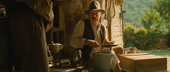 Movie still from “Jean de Florette” (1986), directed by Claude Berri – An old man in a hat and a vest cutting a piece of food; Medium shot, Low angle