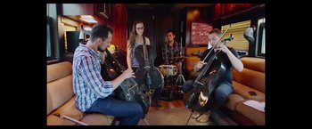 Movie still from “Jem and the Holograms” (2015), directed by Jon M. Chu – A group of people sitting in a room playing musical instruments; Wide shot, Low angle