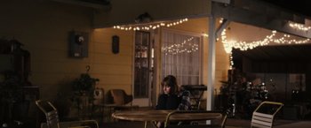 Movie still from “Jem and the Holograms” (2015), directed by Jon M. Chu – A woman sitting at a table in front of lights; Wide shot, High angle