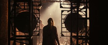 Movie still from “Jem and the Holograms” (2015), directed by Jon M. Chu – A woman is standing in front of stage lights; Wide shot, Over the shoulder angle