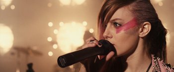 Movie still from “Jem and the Holograms” (2015), directed by Jon M. Chu – A woman holding a microphone up to her mouth; Close Up shot, Over the shoulder angle