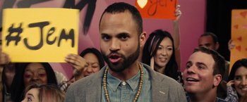 Movie still from “Jem and the Holograms” (2015), directed by Jon M. Chu – A man with a beard is standing in front of a group of people; Close Up shot, Over the shoulder angle