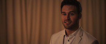 Movie still from “Jem and the Holograms” (2015), directed by Jon M. Chu – A man wearing a white suit jacket and a white shirt; Close Up shot, Over the shoulder angle