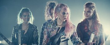 Movie still from “Jem and the Holograms” (2015), directed by Jon M. Chu – A group of people that are standing in a room together; Medium shot, Over the shoulder angle