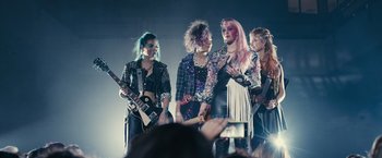 Movie still from “Jem and the Holograms” (2015), directed by Jon M. Chu – A group of young people standing next to each other on a stage; Medium shot, Low angle