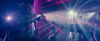 Movie still from “Jem and the Holograms” (2015), directed by Jon M. Chu – A woman in a white dress is playing a guitar; Wide shot, Low angle