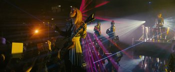 Movie still from “Jem and the Holograms” (2015), directed by Jon M. Chu – A woman in a yellow and black dress holding a guitar; Wide shot, Low angle
