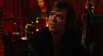Movie still from “Jennifer's Body” (2009), directed by Karyn Kusama – A man sitting in front of a microphone in front of a band; Close Up shot, Over the shoulder angle