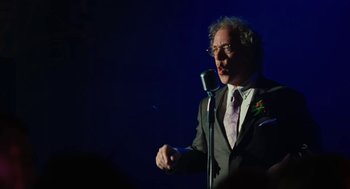 Movie still from “Jennifer's Body” (2009), directed by Karyn Kusama – A man in a suit and tie holding a microphone; Medium shot, Over the shoulder angle