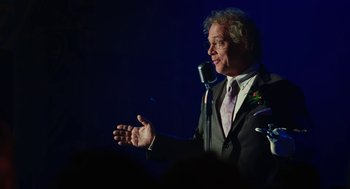 Movie still from “Jennifer's Body” (2009), directed by Karyn Kusama – A man in a suit and tie is speaking into a microphone; Medium shot, Over the shoulder angle