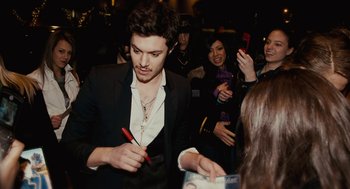 Movie still from “Jennifer's Body” (2009), directed by Karyn Kusama – A man holding a red pen in front of a group of people; Medium shot, Overhead angle