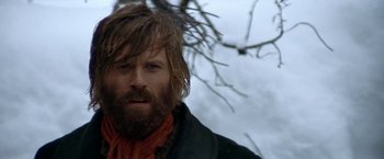 Movie still from “Jeremiah Johnson” (1972), directed by Sydney Pollack – A man with long hair and a beard standing next to a tree; Close Up shot, Low angle
