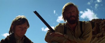 Movie still from “Jeremiah Johnson” (1972), directed by Sydney Pollack – A man with a beard holding a stick in his hands; Medium shot, Low angle