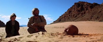 Movie still from “Jeremiah Johnson” (1972), directed by Sydney Pollack – An old man laying in the sand next to an older man; Wide shot, Low angle