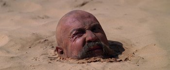 Movie still from “Jeremiah Johnson” (1972), directed by Sydney Pollack – An old man with a beard and a mustache is buried in the sand; Close Up shot, High angle