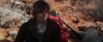 Movie still from “Jeremiah Johnson” (1972), directed by Sydney Pollack – A young man sitting on the ground in the dirt; Medium shot, Over the shoulder angle