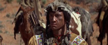 Movie still from “Jeremiah Johnson” (1972), directed by Sydney Pollack – A man in a native american outfit holding a bow and arrow; Close Up shot, Low angle