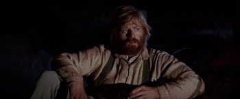 Movie still from “Jeremiah Johnson” (1972), directed by Sydney Pollack – A man with long hair and a beard is sitting in the dark; Close Up shot, Low angle