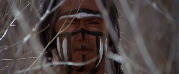 Movie still from “Jeremiah Johnson” (1972), directed by Sydney Pollack – A man with a painted face looking at the camera through a fence; Close Up shot, Low angle