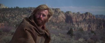 Movie still from “Jeremiah Johnson” (1972), directed by Sydney Pollack – A man with long hair and a beard is standing in the desert; Close Up shot, Low angle