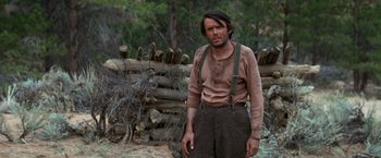 Movie still from “Jeremiah Johnson” (1972), directed by Sydney Pollack – A man standing in the woods wearing a brown shirt and suspenders; Medium shot, Low angle