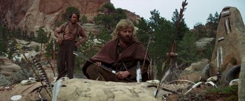 Movie still from “Jeremiah Johnson” (1972), directed by Sydney Pollack – A man sitting on the ground holding a spear; Medium shot, Over the shoulder angle