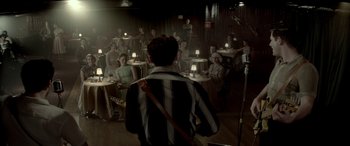 Movie still from “Jersey Boys” (2014), directed by Clint Eastwood – A group of people sitting in a room with lights on; Wide shot, Over the shoulder angle