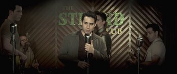 Movie still from “Jersey Boys” (2014), directed by Clint Eastwood – A man holding a microphone while standing next to another man; Medium shot, Low angle