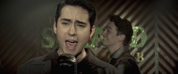 Movie still from “Jersey Boys” (2014), directed by Clint Eastwood – A man singing into a microphone while another man looks on; Close Up shot, High angle