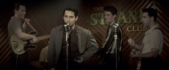 Movie still from “Jersey Boys” (2014), directed by Clint Eastwood – Two men are singing into microphones in front of a wooden wall; Medium shot, Over the shoulder angle