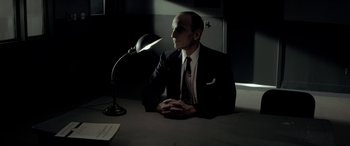 Movie still from “Jersey Boys” (2014), directed by Clint Eastwood – A man sitting at a table with a lamp in front of him; Medium shot, Low angle