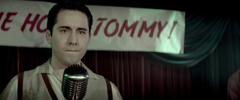 Movie still from “Jersey Boys” (2014), directed by Clint Eastwood – A man holding a microphone in front of a banner; Close Up shot, Low angle