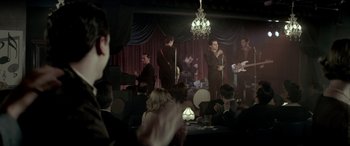 Movie still from “Jersey Boys” (2014), directed by Clint Eastwood – A group of people sitting at a table with microphones; Wide shot, Over the shoulder angle