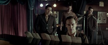 Movie still from “Jersey Boys” (2014), directed by Clint Eastwood – A group of men standing next to each other in a room; Medium shot, Low angle