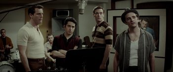 Movie still from “Jersey Boys” (2014), directed by Clint Eastwood – A group of young men standing next to each other in a room; Medium shot, Over the shoulder angle