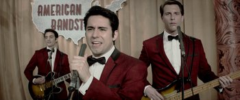 Movie still from “Jersey Boys” (2014), directed by Clint Eastwood – A man in a red jacket holding a microphone and another man in a red jacket holding a guitar; Close Up shot, Over the shoulder angle